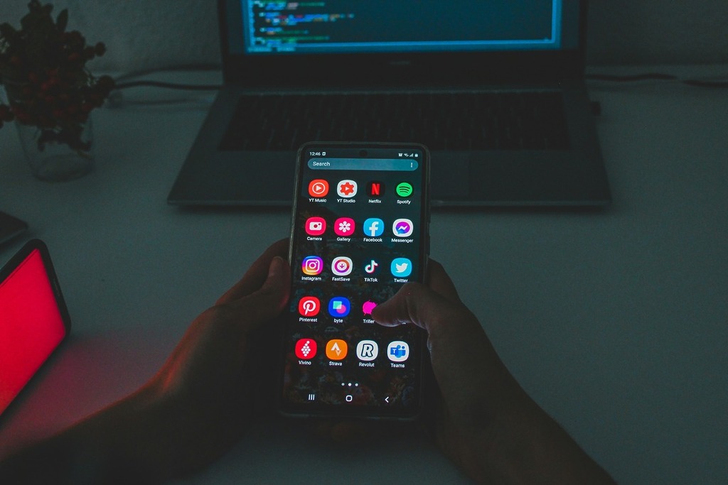 Android phone with laptop coding in background.