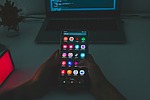 Android phone with laptop coding in background.