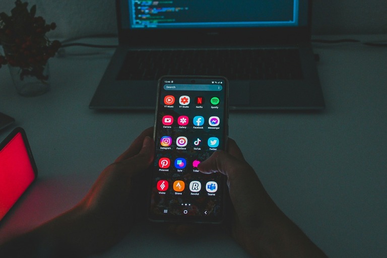 Android phone with laptop coding in background.